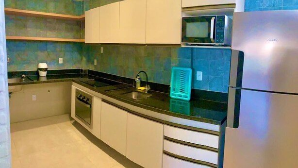 Una cocina con armarios blancos, encimera negra, microondas y refrigerador.