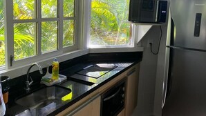 Una cocina con un refrigerador de acero inoxidable, un microondas y un lavamanos con una ventana arriba.
