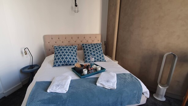 Un lit bien fait, doté d’une tête de lit capitonnée, de deux coussins à motifs, d’un plateau avec des articles de toilette et de deux serviettes.
