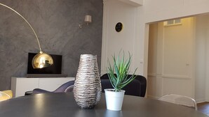 Un espace repas moderne avec une table ronde, un vase à texture, une plante en pot et une suspension dorée.