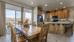 Un comedor amplio con una gran mesa y sillas de madera, una cocina con muebles y electrodomésticos de madera, y vistas al paisaje a través de amplias ventanas.