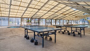 Un espacio interior techado con varias mesas de ping pong y una piscina.