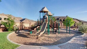 Un parque infantil con tobogán y estructuras para escalar, rodeado de un área ajardinada con un camino de grava y follaje.