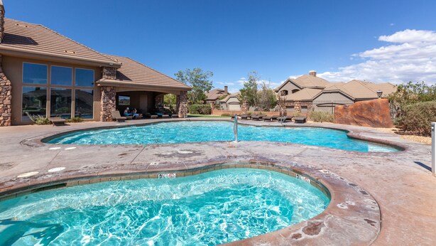 Una piscina residencial con hidromasaje, detalles de piedra y un cielo azul despejado.