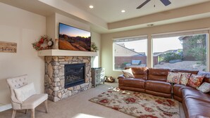 Una sala de estar con chimenea de piedra, un sofá de cuero, un sillón blanco y un ventanal con vistas al exterior.