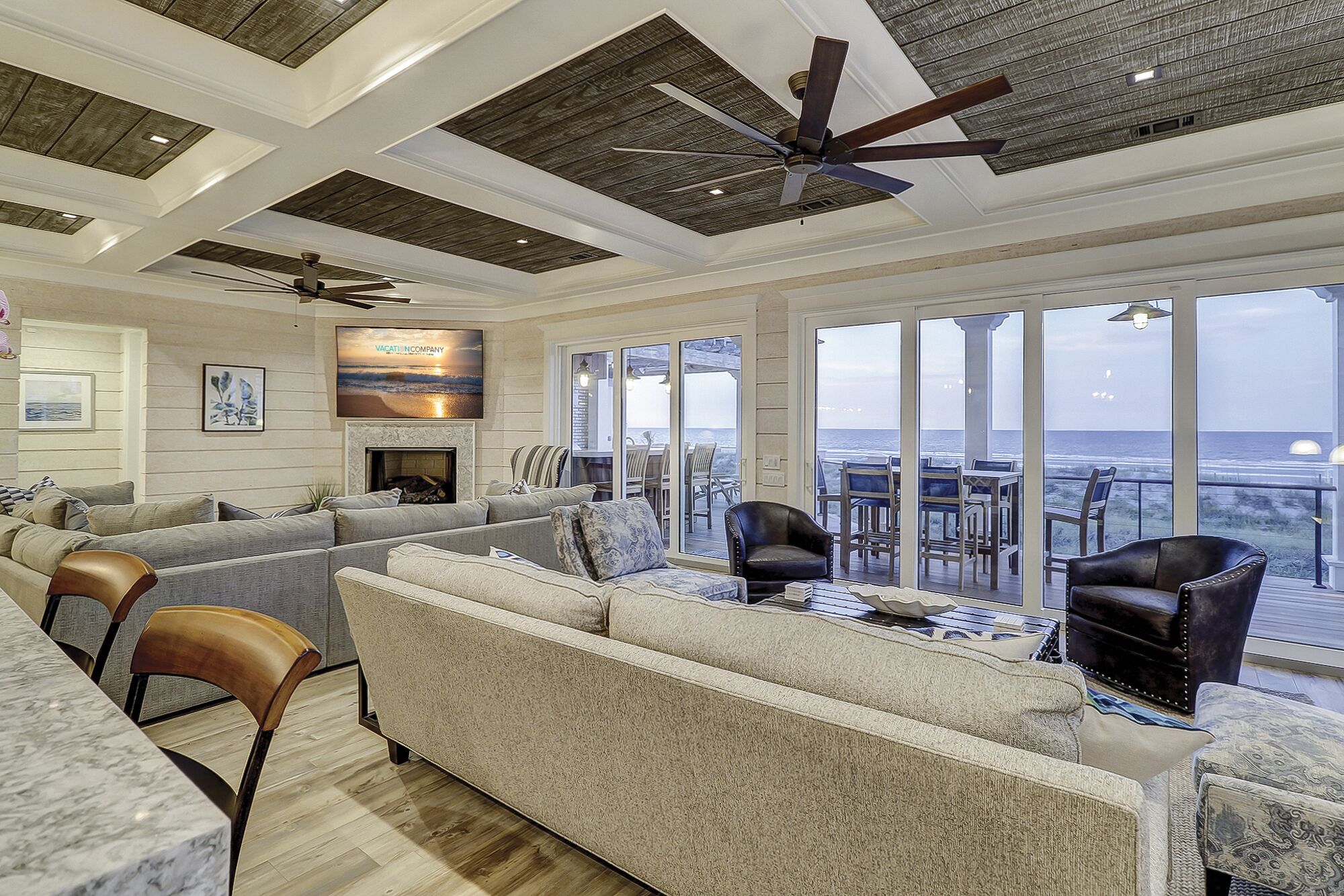 A spacious living area with a large sofa, a fireplace, and a view of the ocean through large sliding glass doors.