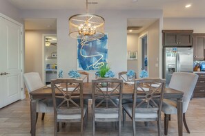 A dining area with a wooden table and chairs, a chandelier, and a blue abstract painting on the wall.