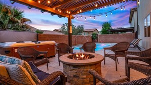An outdoor patio with a stone fire pit, wicker furniture, and a hot tub. - 94 PV, Luxury Home with Private Pool & Hot Tub, Fire Pit, Huge Kitchen, and More! (Santa Clara)