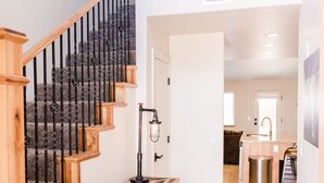 Un escalier avec des marches en bois et des rampes noires, menant à un coin cuisine équipé d’un évier et d’une poubelle.