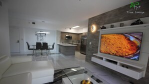 Een moderne woonkamer met een witte bank, een glazen salontafel en een flatscreen televisie aan de wand.