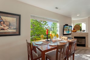 Uma sala de jantar com uma mesa posta para quatro pessoas, lareira e uma grande janela com vista para o verde.