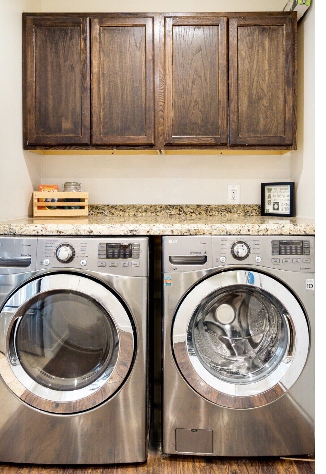 A laundry area with two stainless steel front-loading washers and dark wooden cabinets above.