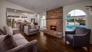 A spacious living room with a stone fireplace, two armchairs, and a view of a pool through a large arched window. - Kierland Retreat w/Heated Pool & Outdoor Fireplace  (Scottsdale)