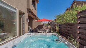Un espace spa comprenant un jacuzzi, des sièges extérieurs et un parasol rouge.