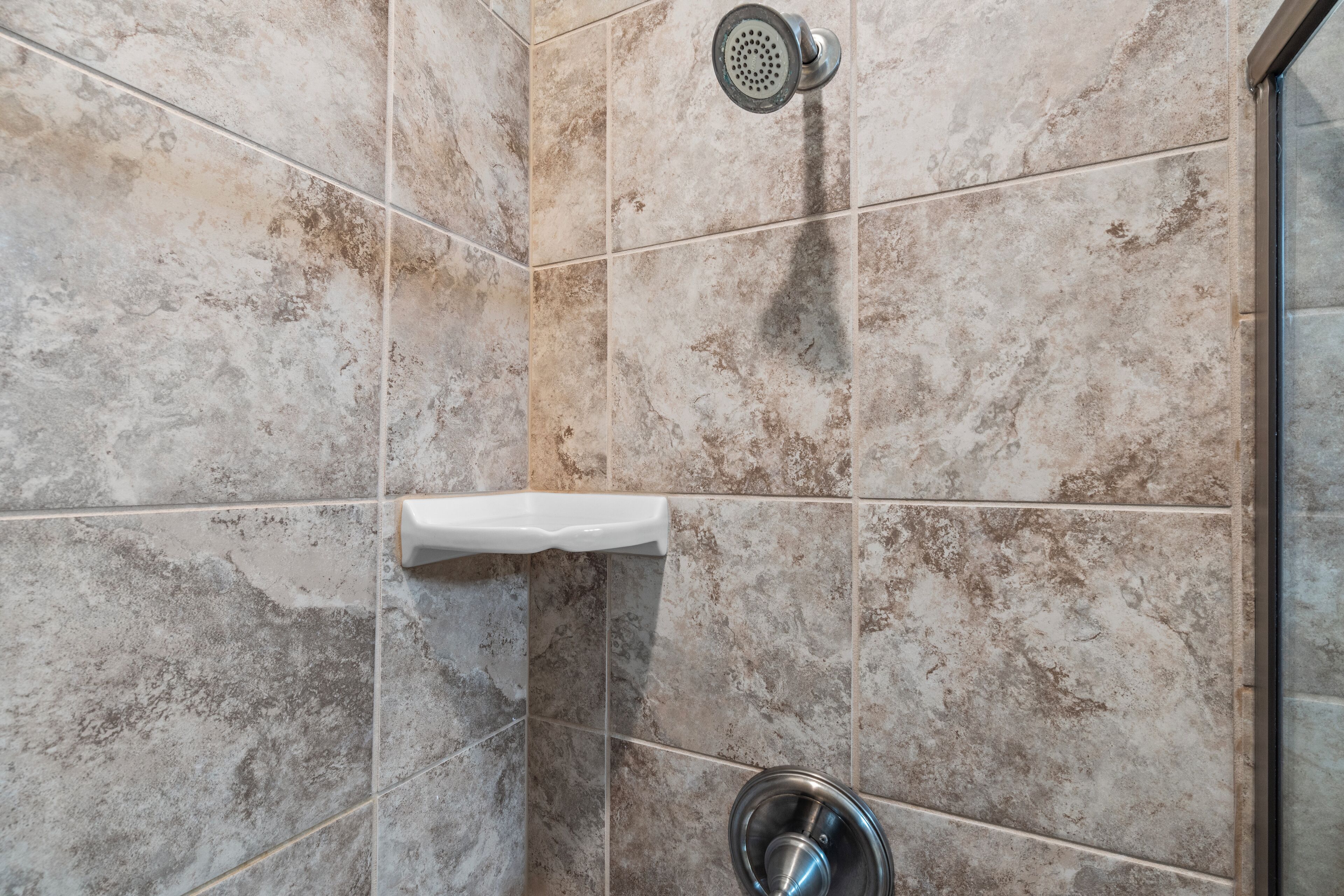 Uma casa de banho com azulejos bege, um chuveiro e uma pia de aço inoxidável.