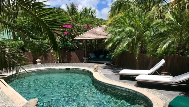 Una piscina cristalina con borde curvo, rodeada de sillas de descanso y una terraza de madera.