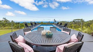 A poolside area with a round table and chairs, a pool, and a view of the ocean.