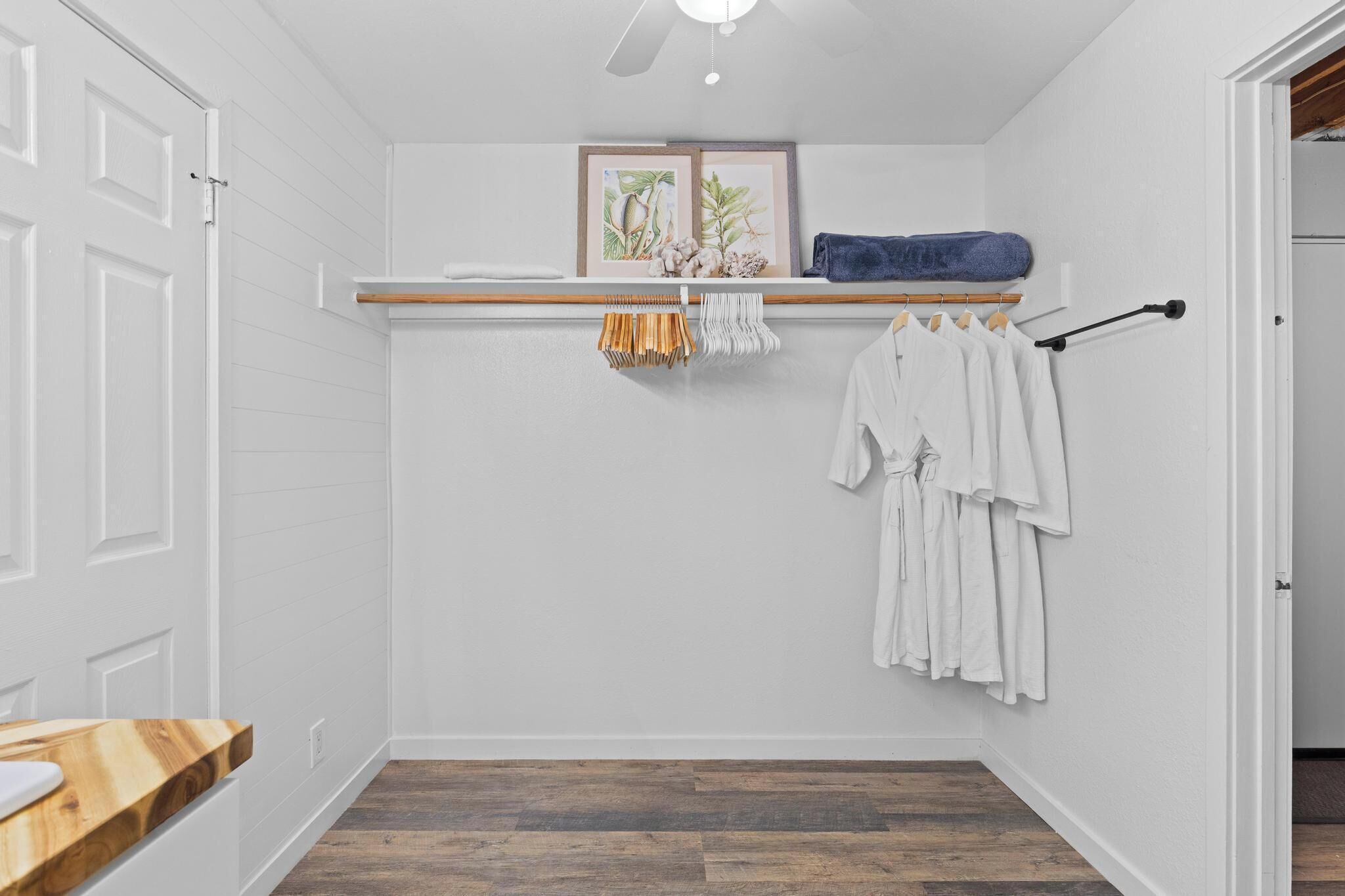 A small, clean bathroom with a wooden vanity, a towel rack with white towels, and a framed botanical print on the wall.