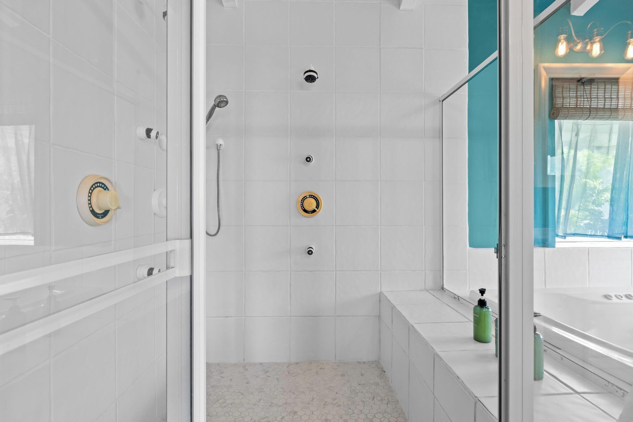 A modern bathroom with a glass shower enclosure, white tiled walls, and a bathtub with a green bottle on the side.
