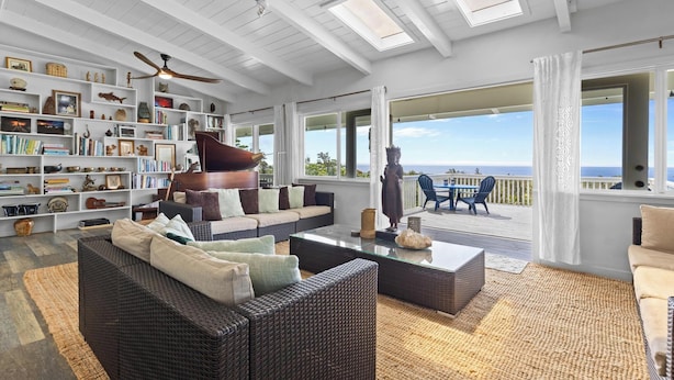 A spacious living room with a large bookshelf, comfortable seating, and a view of the ocean.
