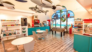 A restaurant with a wooden floor, white tables, and chairs. There are shelves with snacks and a Coca-Cola machine. - Las Palmas Resort 304, Main Level Condo, New Flooring, Mountain Views, Close to Pools, and more (St. George)