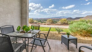 An outdoor patio with a table and chairs, a small table with a plant, and a view of a desert landscape with mountains in the distance. - Las Palmas Resort 304, Main Level Condo, New Flooring, Mountain Views, Close to Pools, and more (St. George)