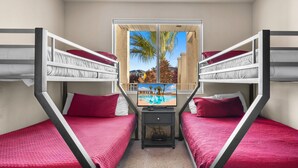Ein Zimmer mit Etagenbetten, einem kleinen Tisch und einem Fenster mit Blick auf einen Pool und Palmen.