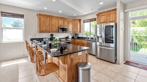 A modern kitchen with wooden cabinets, stainless steel appliances, and a large island with bar stools. - Las Palmas Resort 1805, Resort Access in St George (St. George)