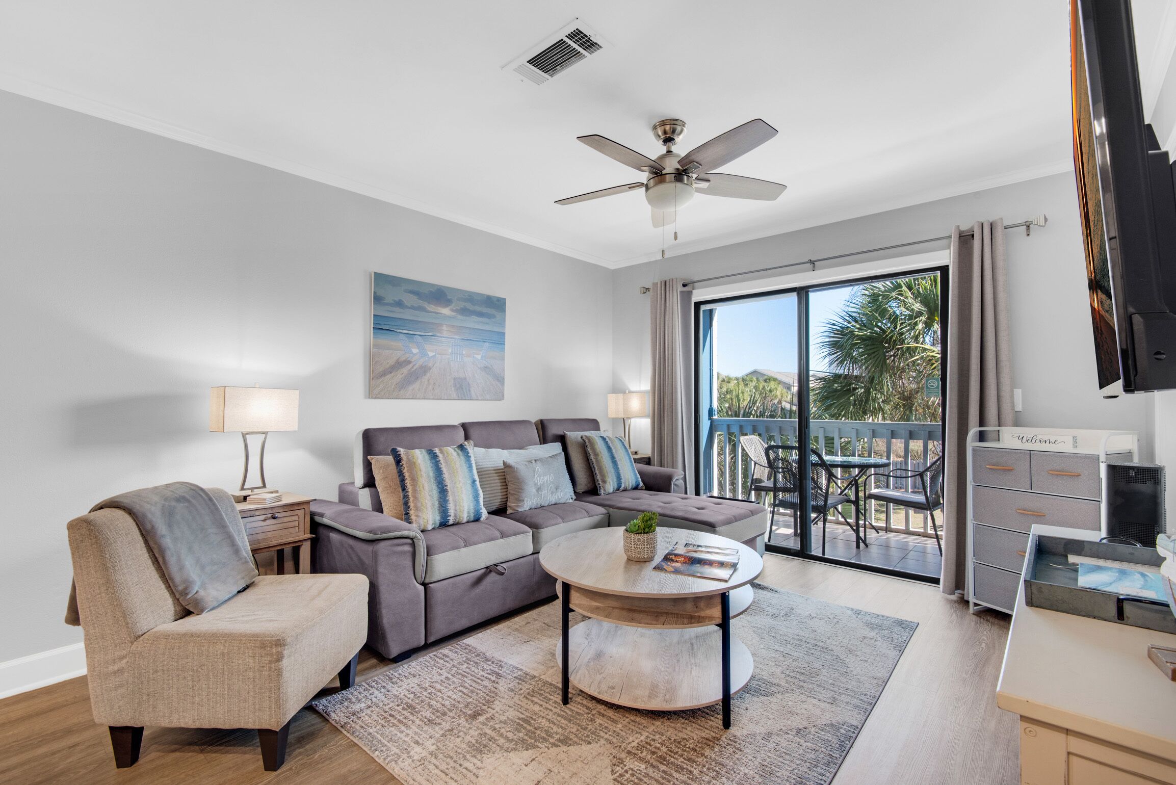 A modern living room with a sofa, armchair, and coffee table, a ceiling fan, and a view to an outdoor patio.