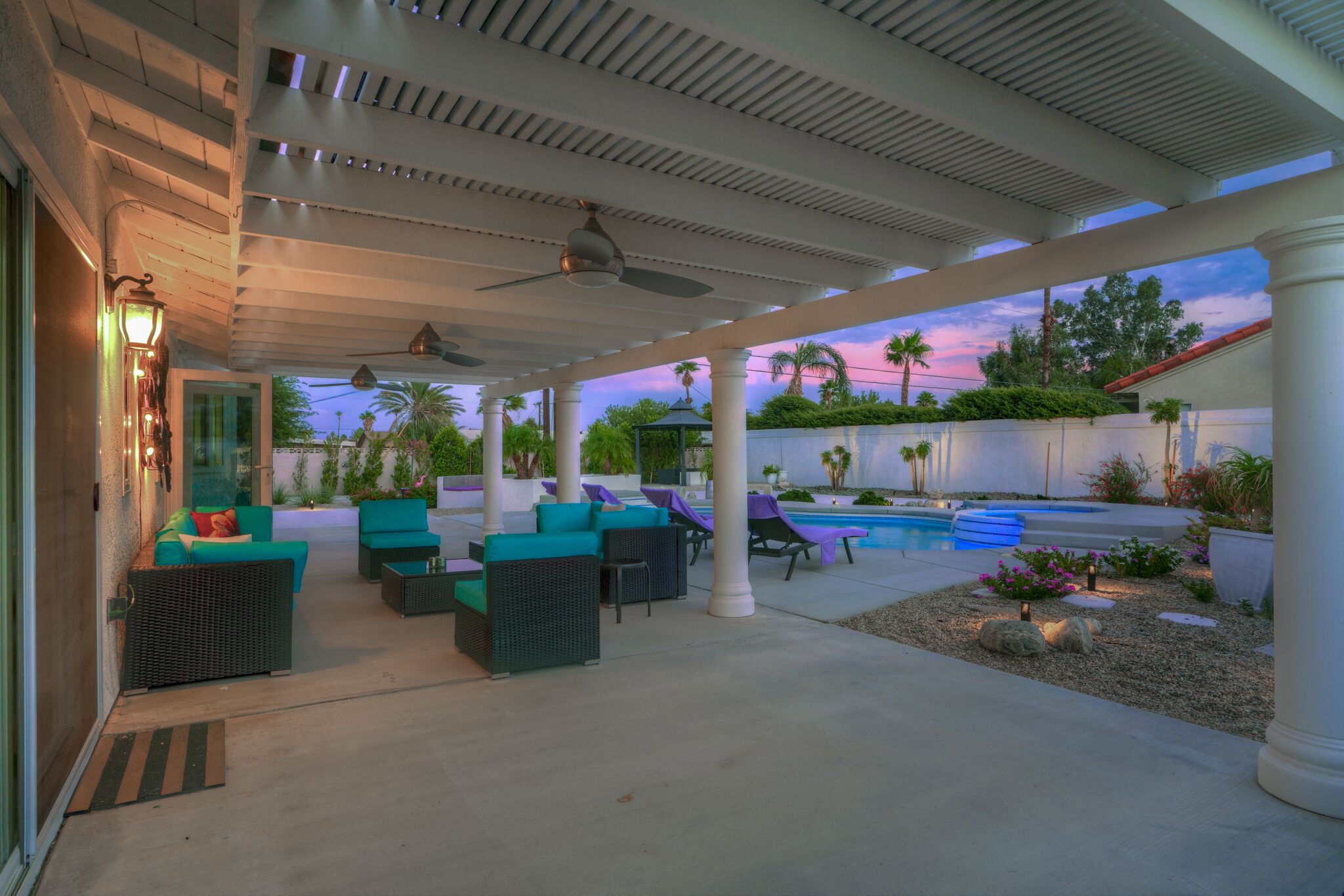 A covered outdoor area with seating, a pool, and a view of the sunset.