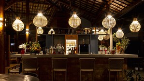 A bar area with wicker chairs, a bar counter with bottles, and hanging wicker light fixtures. - Pousada Casa de Praia (Mata de São João)