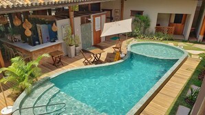 A swimming pool with a wooden deck, lounge chairs, and a bar area with a tiled ceiling. - Pousada Casa de Praia (Mata de São João)