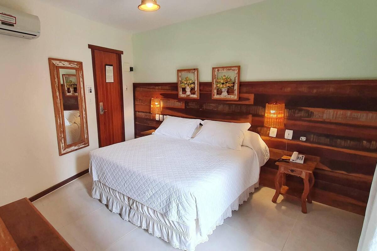 Ein Schlafzimmer mit einem Bett, einem hölzernen Kopfteil, einem Nachttisch mit Lampe und einem Spiegel an der Wand.