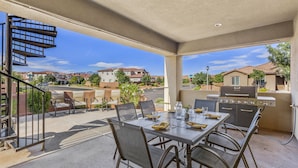Un patio al aire libre con una mesa y sillas, una parrilla y vistas a un barrio residencial.