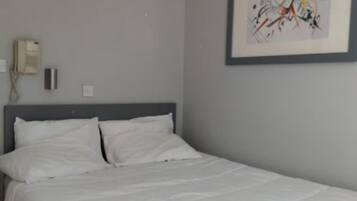 A bedroom with a bed, a wall-mounted telephone, and a framed abstract painting.