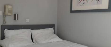 Un dormitorio con una cama, un teléfono instalado en la pared y un cuadro abstracto enmarcado.
