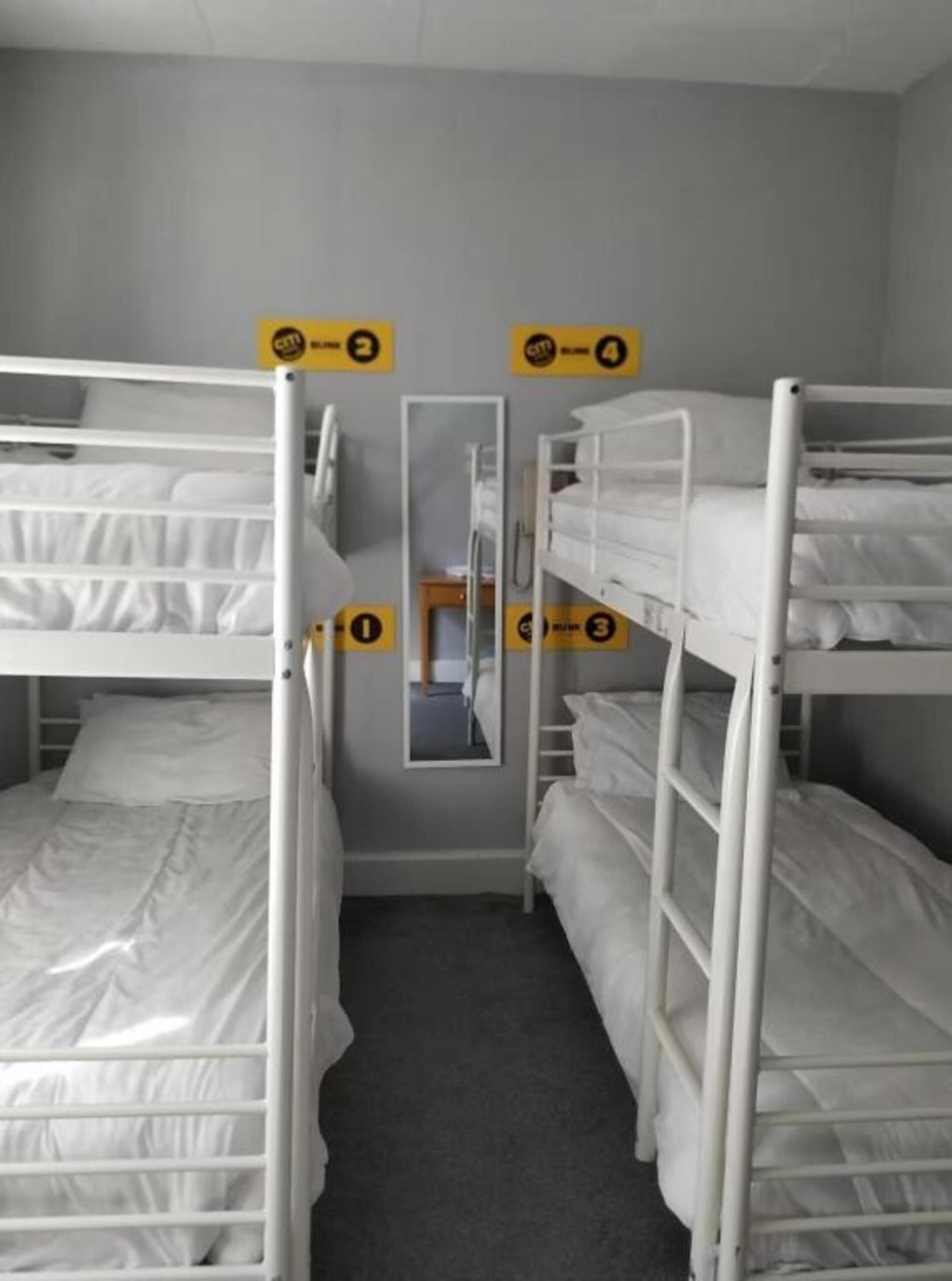 A room with three bunk beds arranged in a row, a small table, and a mirror on the wall.