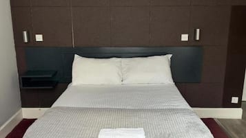 A neatly made bed with a grey and white striped bedspread, a white pillow, and a folded white towel on the bed.