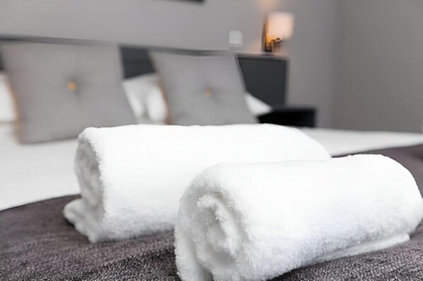 A neatly made bed with two rolled white towels and a modern bedside table with a lamp.