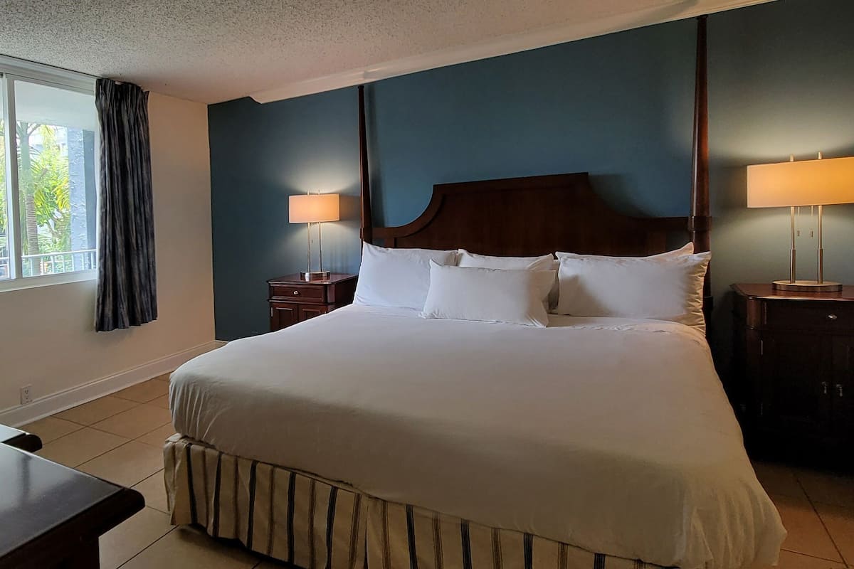 A hotel room with a large bed, two bedside tables with lamps, a desk with a TV, and a window with curtains.