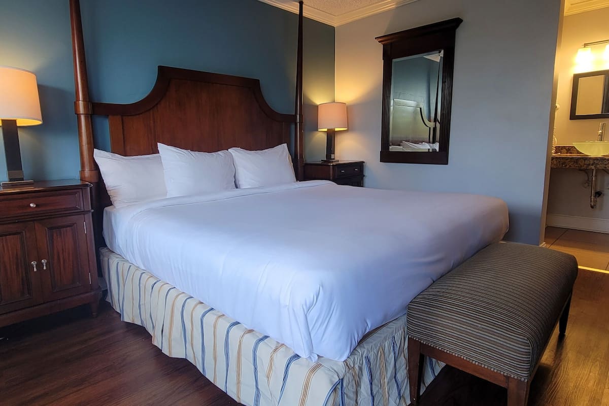 A neatly made bed with white linens, a wooden headboard, and two bedside lamps.