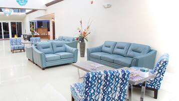 Un hall d’entrée spacieux, avec un canapé bleu, des fauteuils à motifs et une table basse.