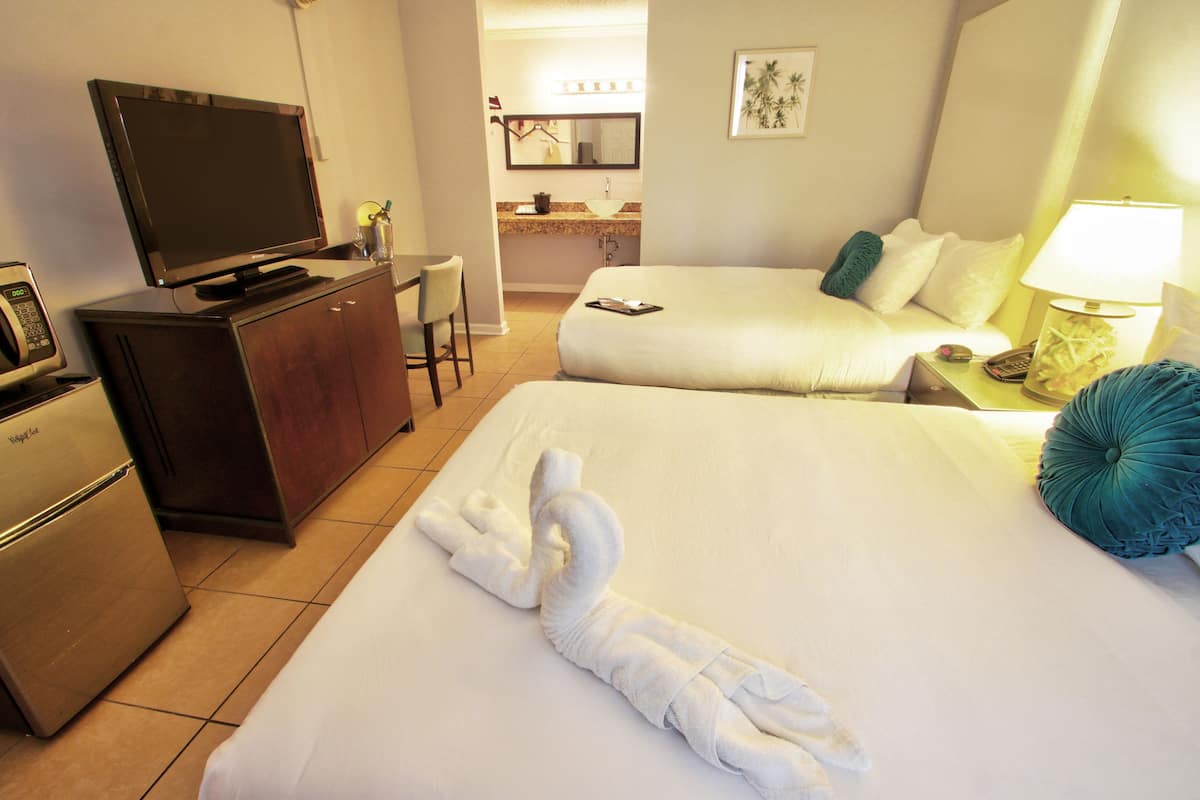 A hotel room with two beds, a TV, a minibar, and a bathroom visible in the background.