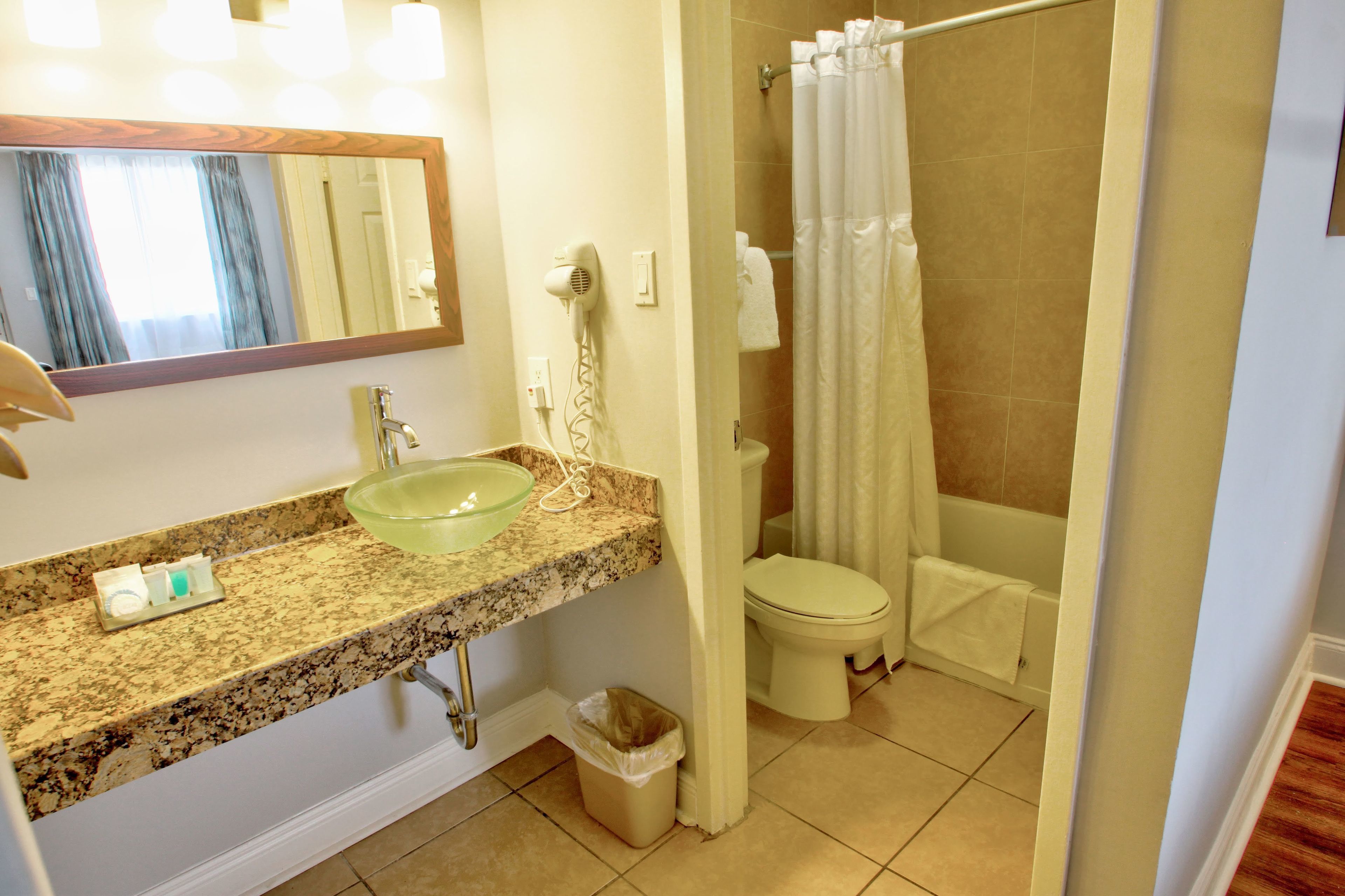A bathroom with a granite countertop sink, a mirror, a hairdryer, a toilet, and a shower curtain.