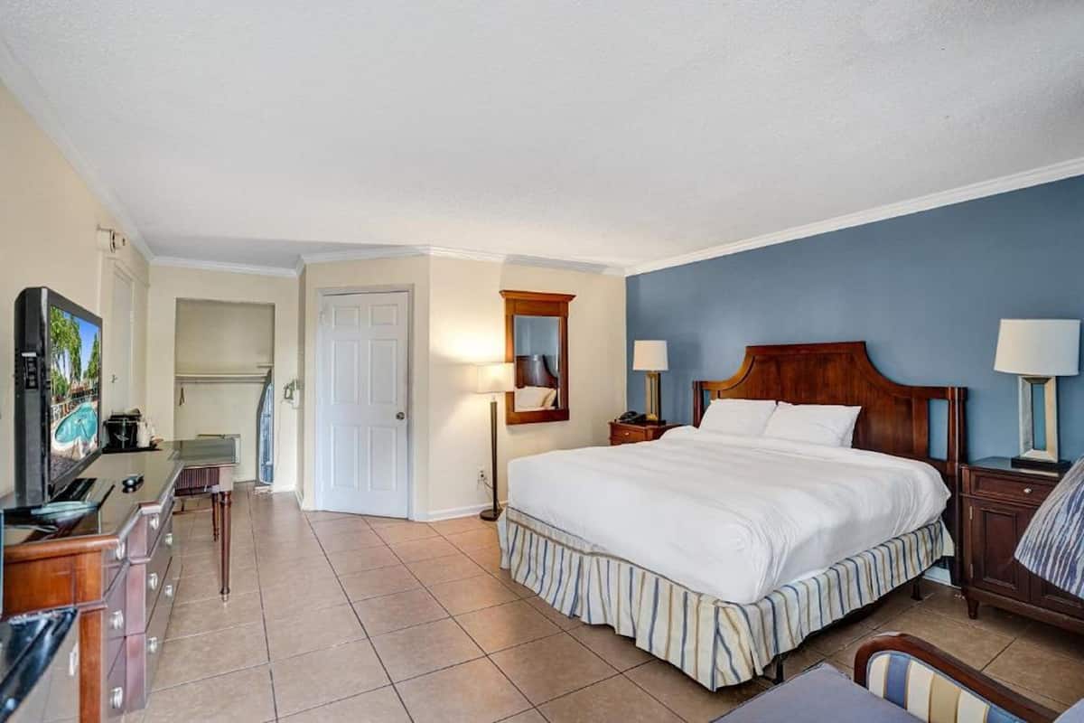 A hotel room with a large bed, a desk with a computer, a TV, and a kitchenette.