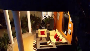 Un espacio al aire libre bien iluminado con sofá y sillones, un felpudo y una escalera que conduce a un nivel superior.