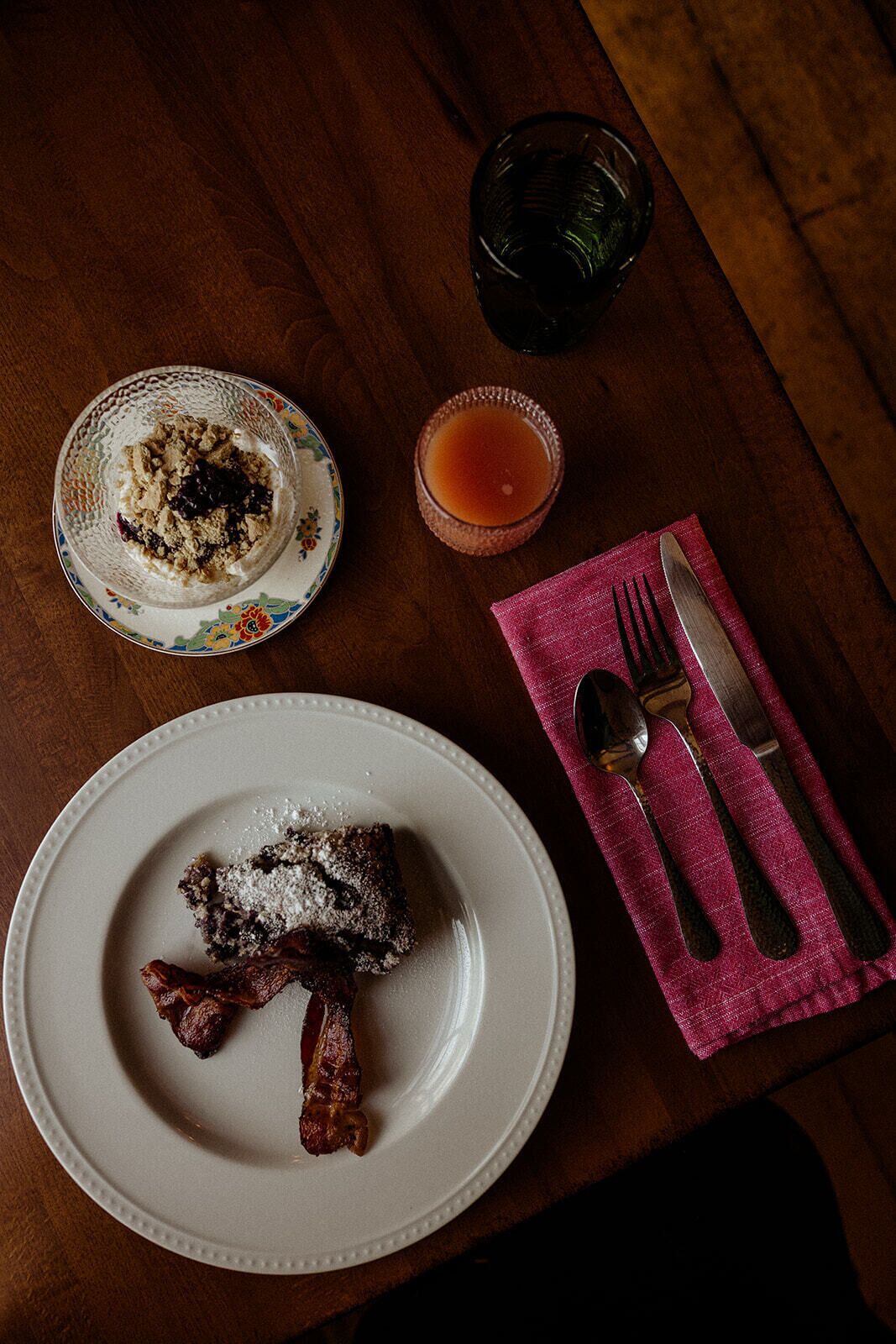 A wooden table with a plate of food, a glass of drink, and cutlery on a napkin.