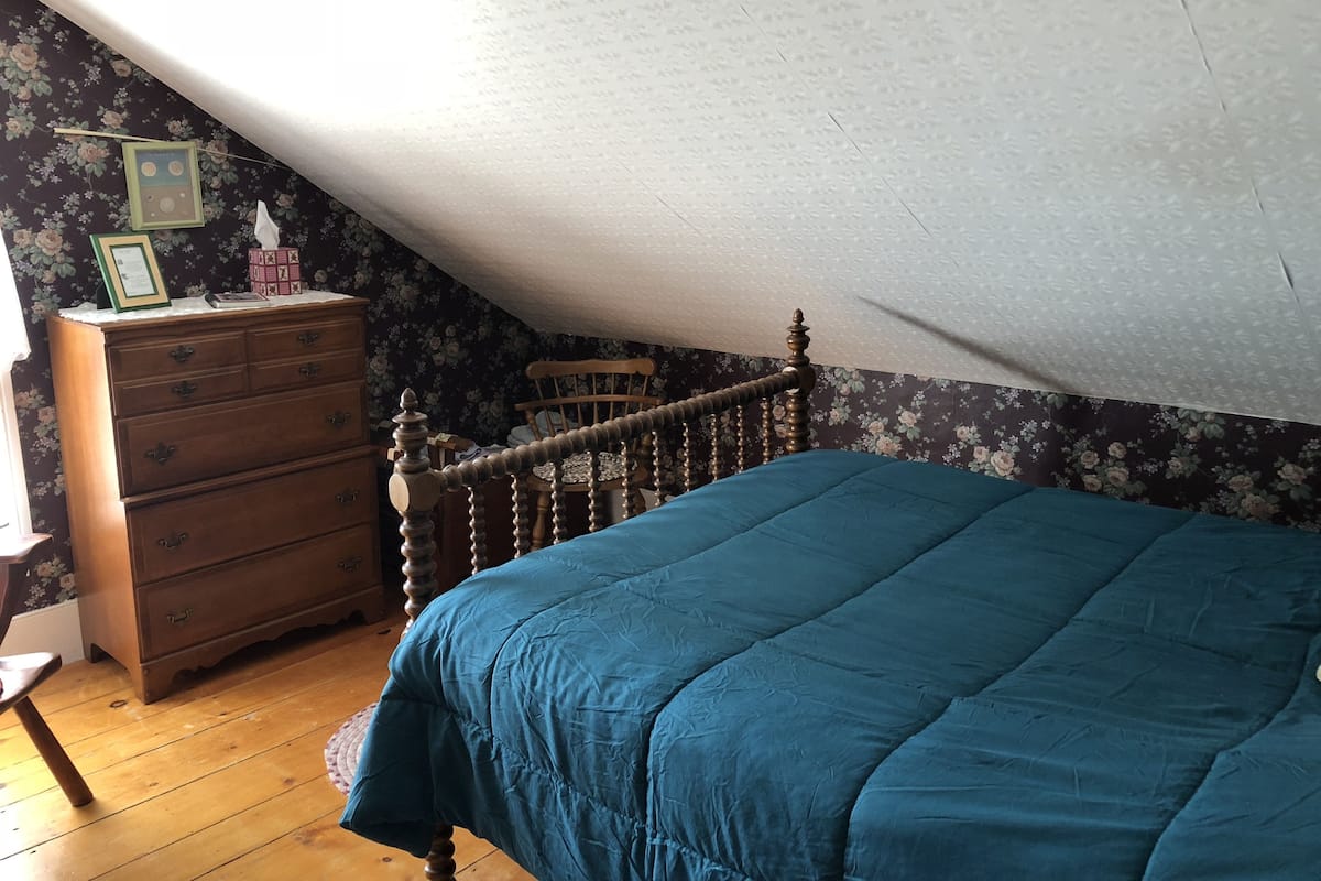 A bedroom with a wooden dresser, a blue bedspread, and floral wallpaper.