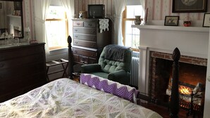 A traditional room with a fireplace, a green armchair, a wooden dresser, and a bed with a quilt. - Mulberry Bed & Breakfast (Wareham)