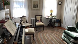 A living room with a piano, two chairs, a table with a lamp, and a radiator. - Mulberry Bed & Breakfast (Wareham)